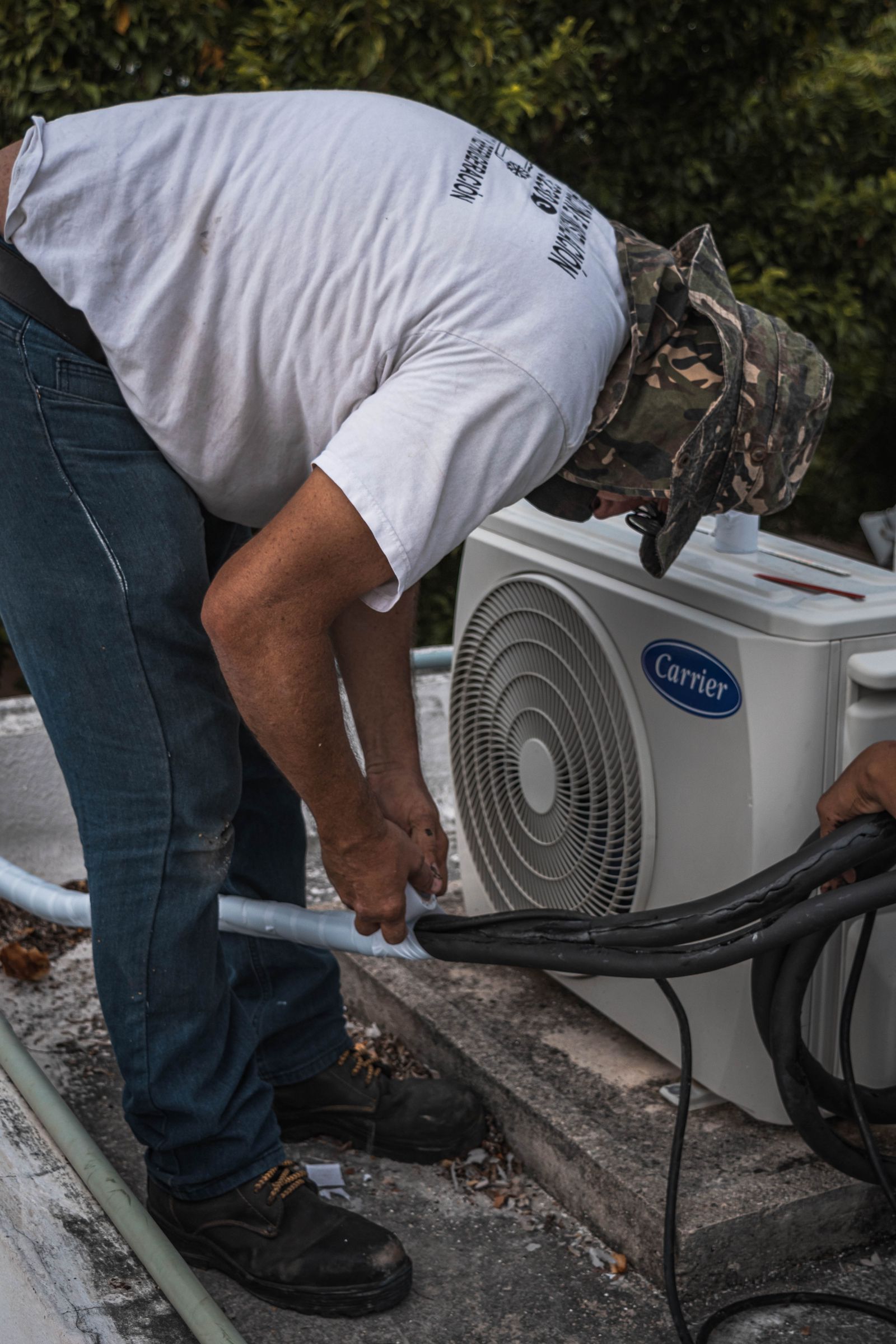 HVAC technician in proper work boots servicing an outdoor Carrier AC condenser unit in Fairfield CT -- Express Home Services