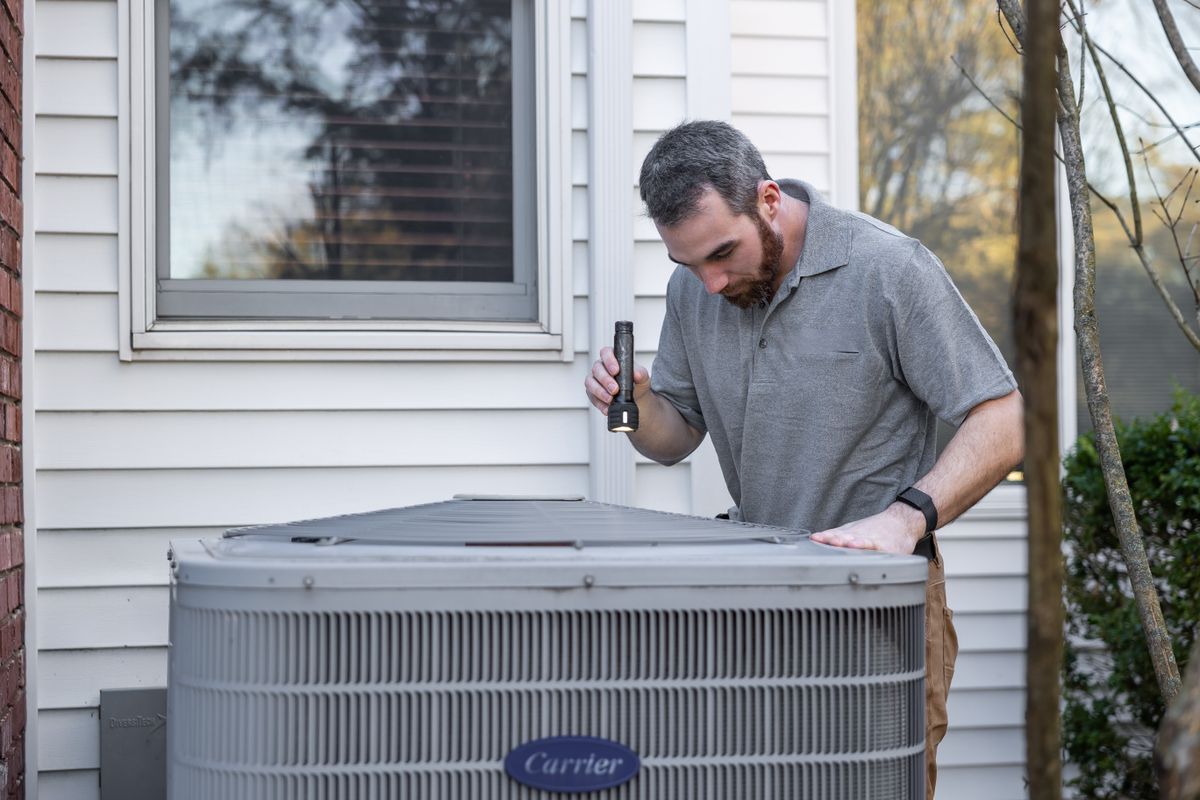 HVAC technician inspecting an outdoor heat pump condensing unit with a flashlight at a Connecticut home -- Express Home Services